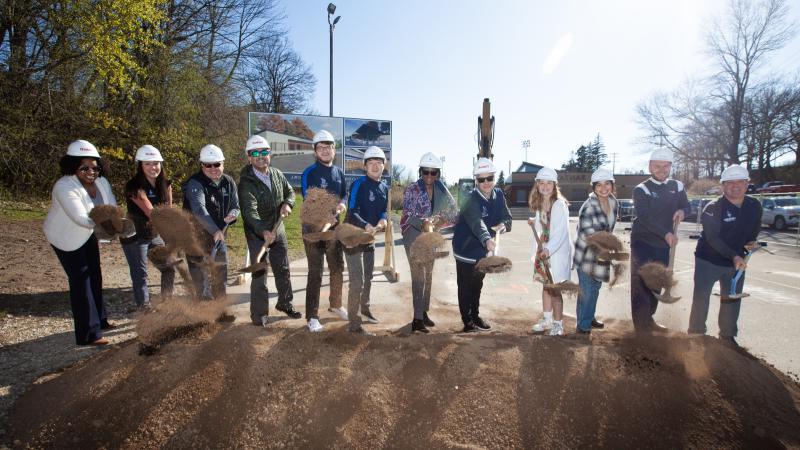 President Laurie Carter leads a group of 11 staff and students in throwing shovels of dirt at the groundbreaking ceremony.